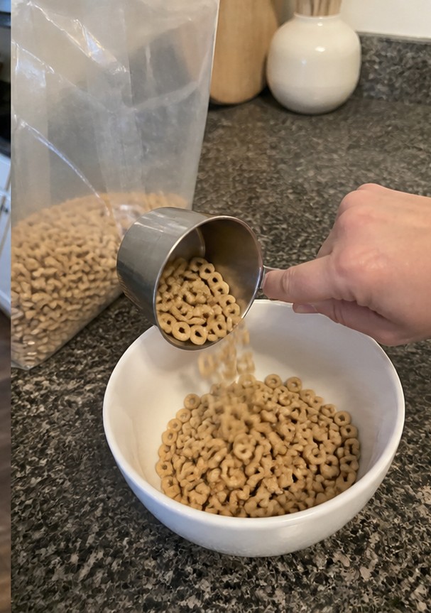 Cereal being poured into a bowl with plain yogurt and banana slices