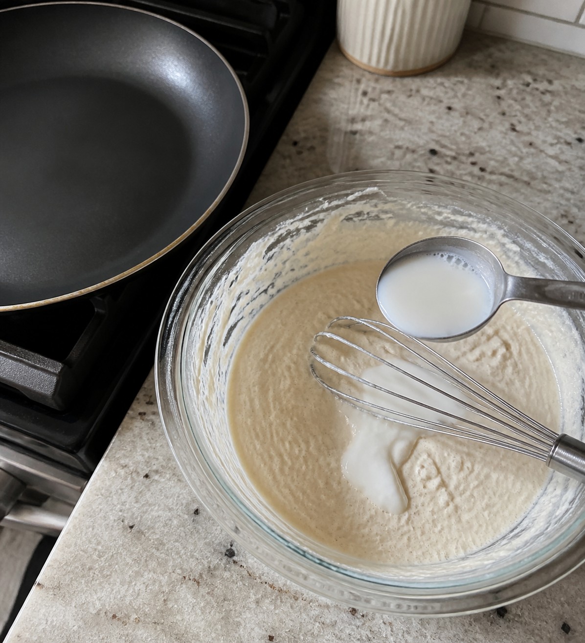 Thick crepe batter being loosened with milk next to a skillet
