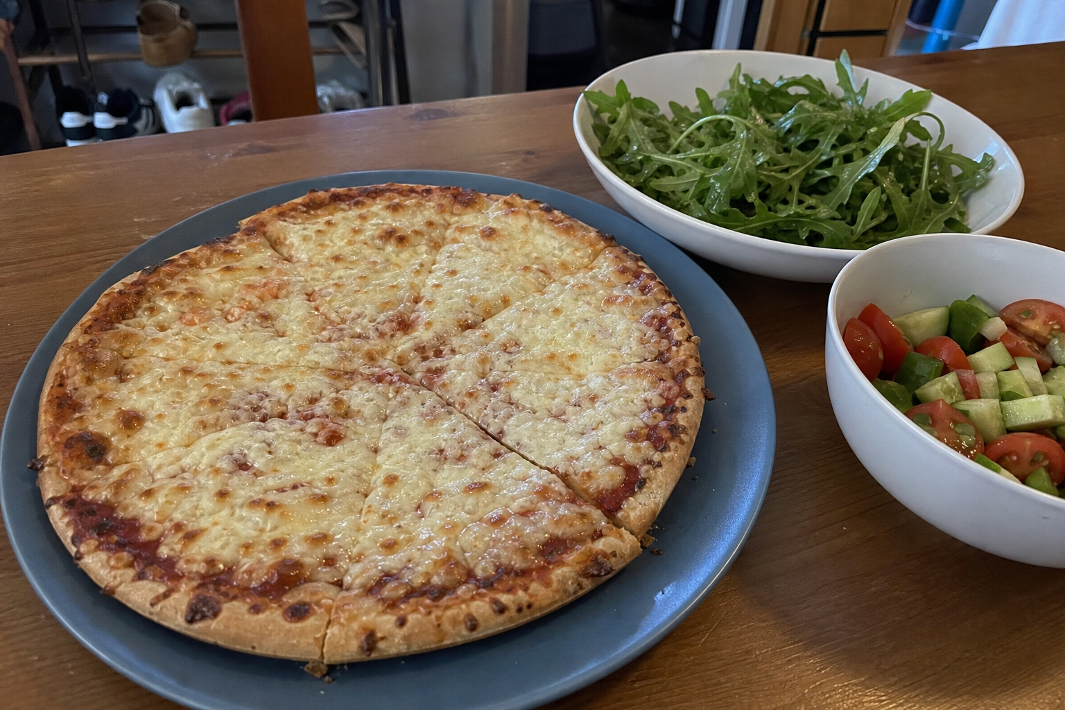 Frozen cheese pizza served with arugula and cucumber tomato salads on a casual kitchen table
