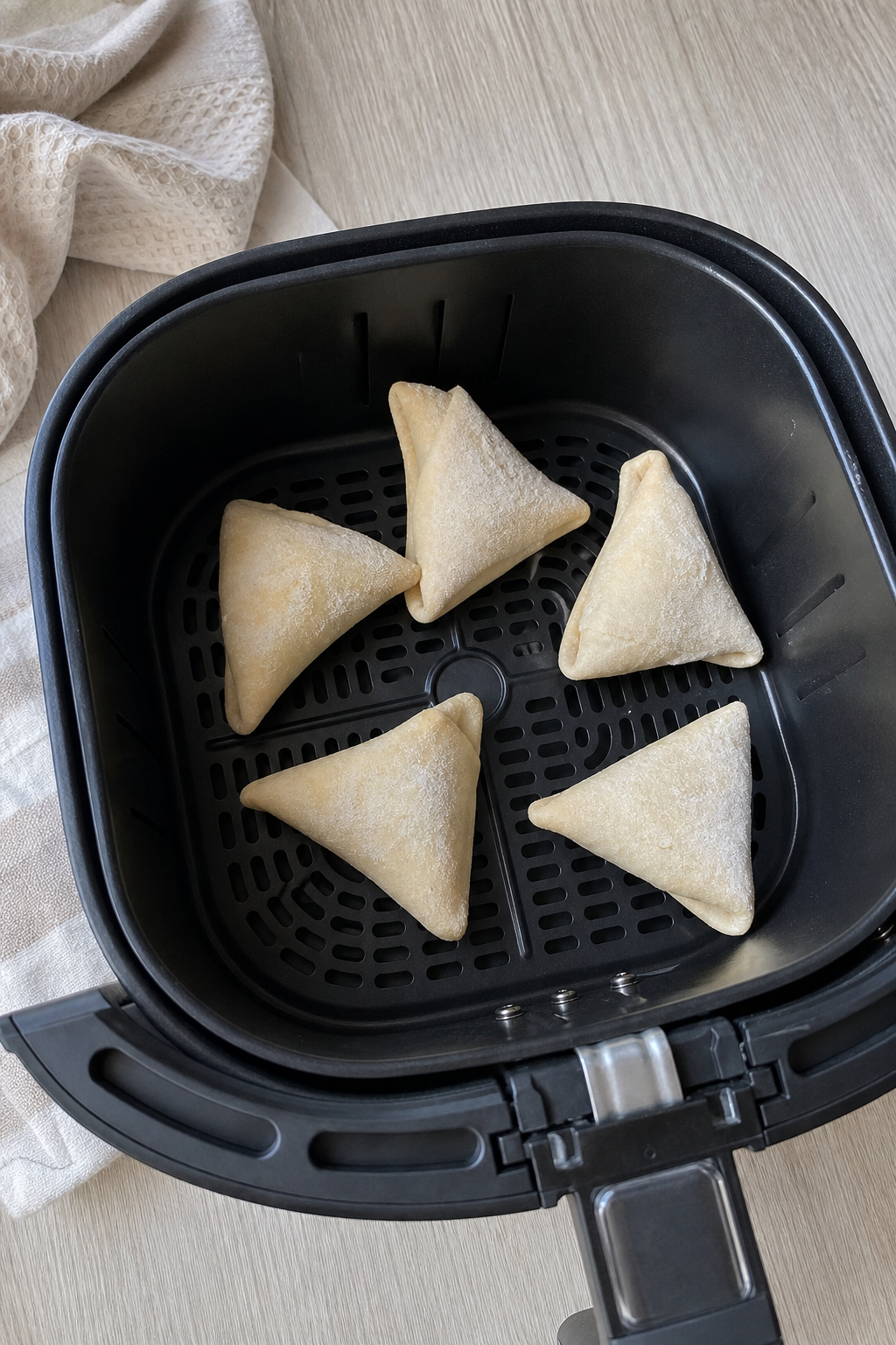 Frozen samosas spaced apart in a black air-fryer basket