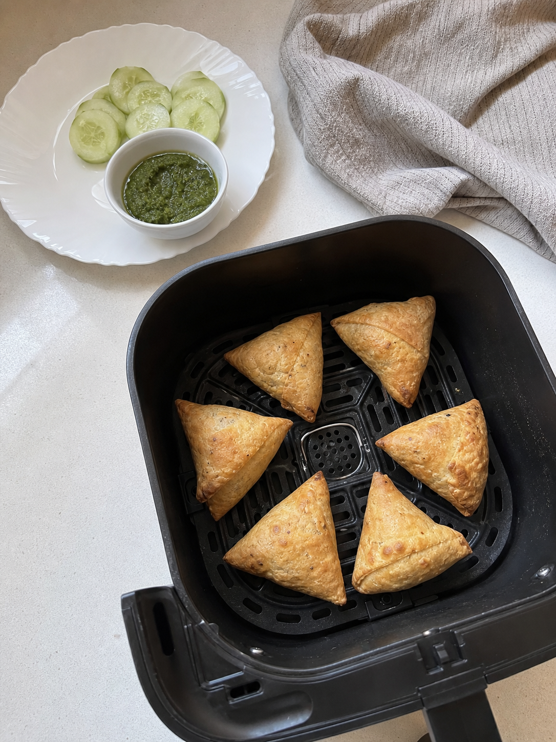 Crisp samosas spaced in an air-fryer basket beside avocado, cucumber and salsa