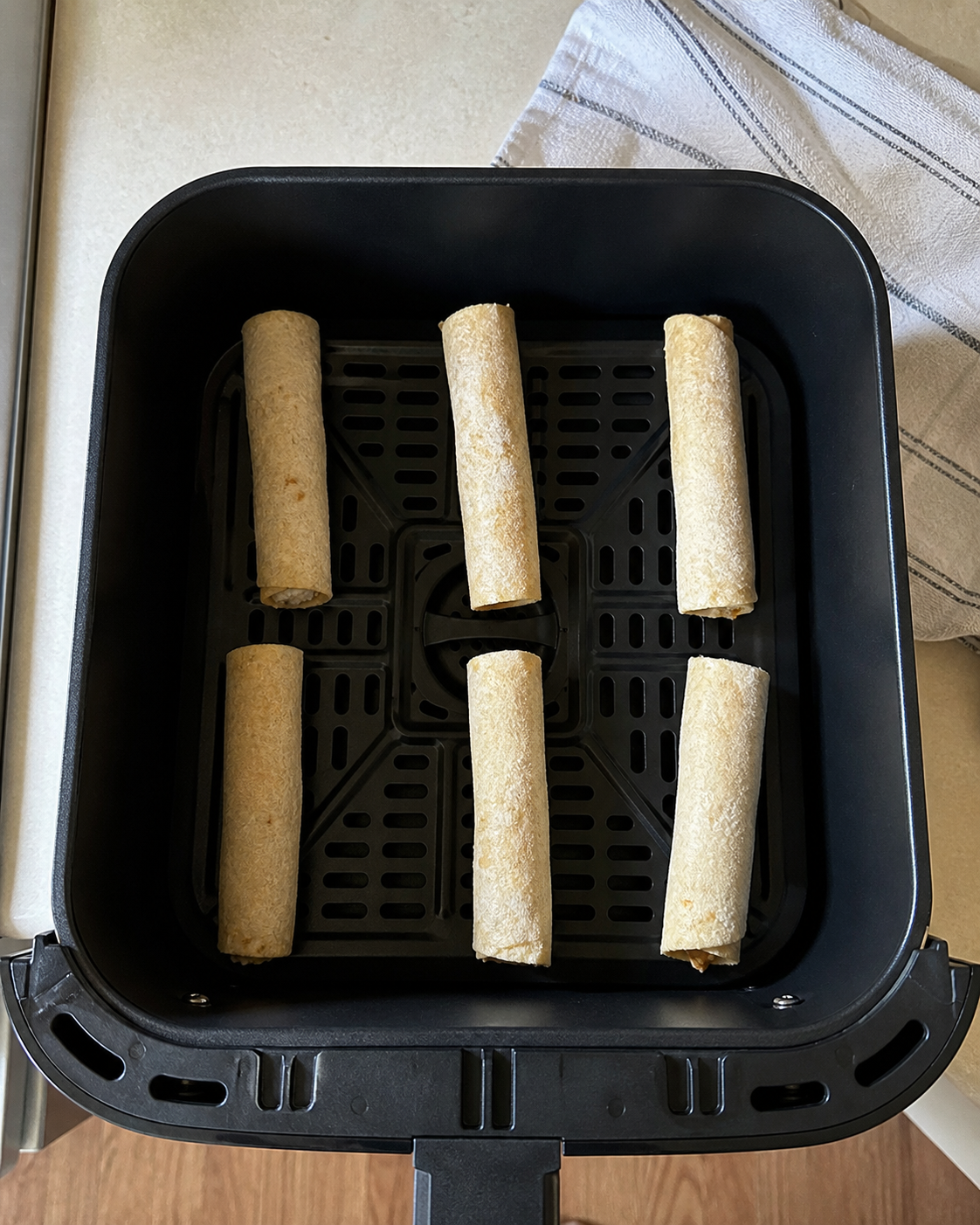 Frozen taquitos spaced apart in a black air-fryer basket
