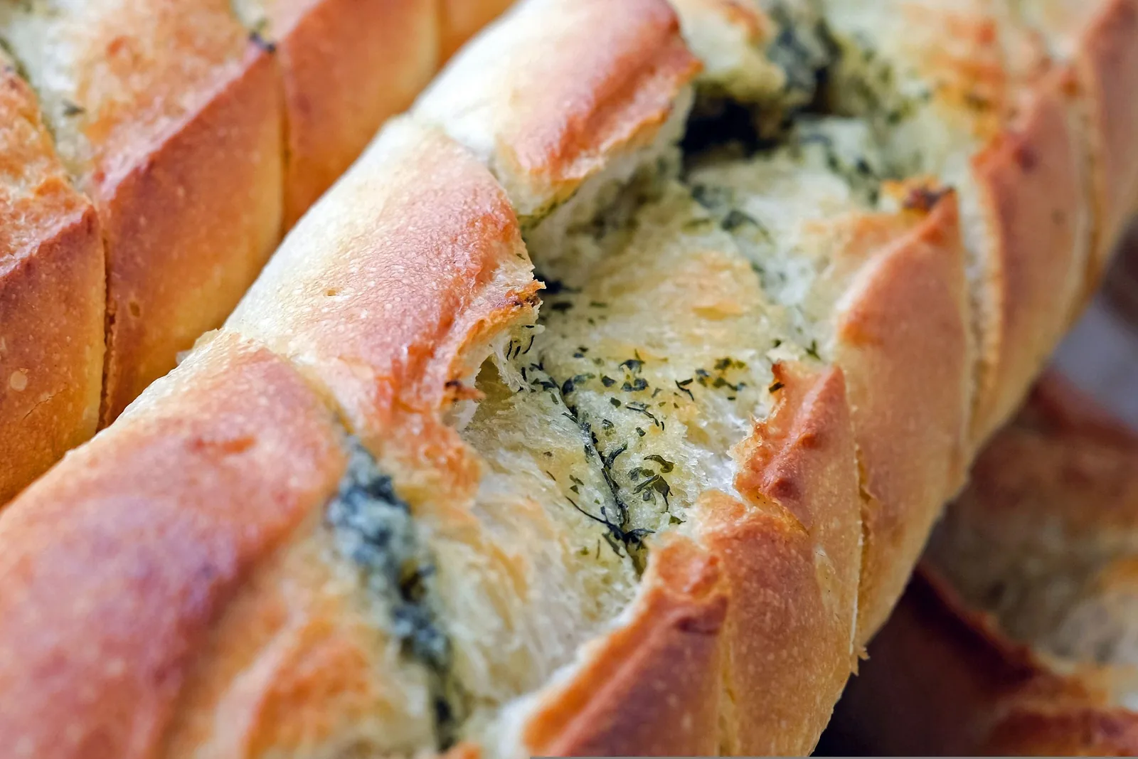 Close-up of golden garlic bread loaves with herb butter between the cuts