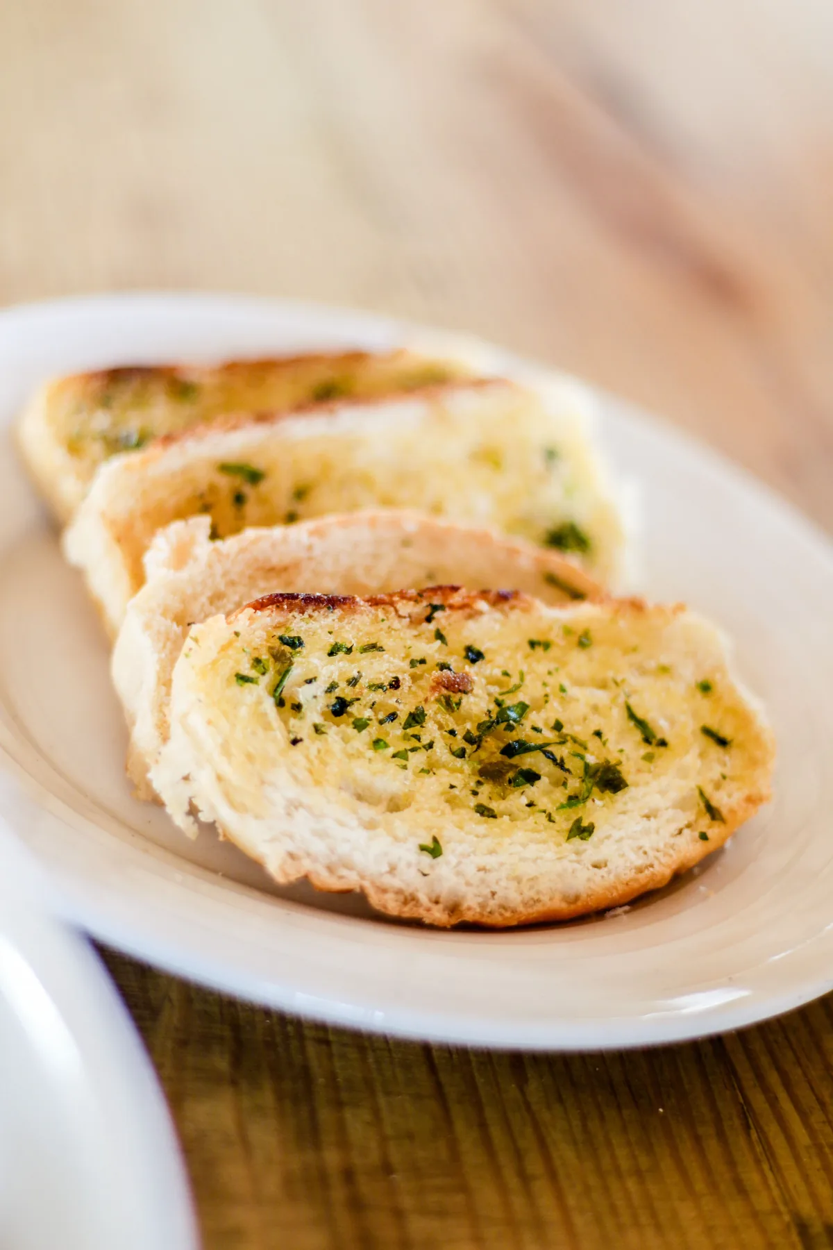Several toasted garlic bread slices with herbs arranged on a white plate
