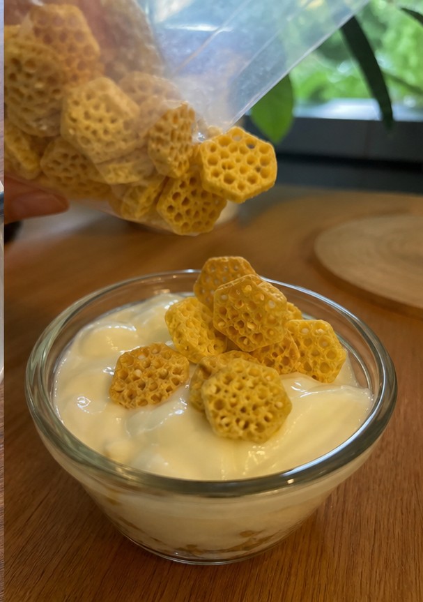 Cereal being poured into a bowl with plain yogurt and banana slices
