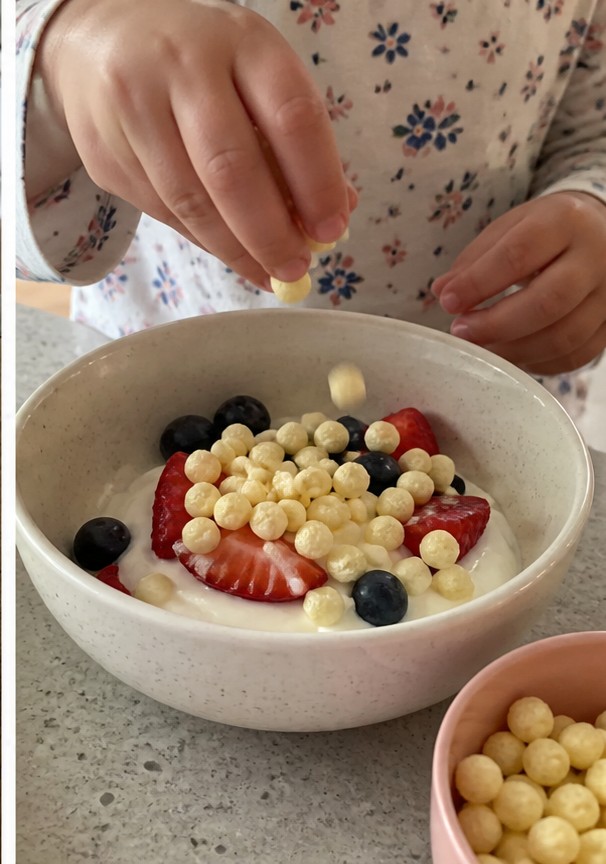 Cereal being poured into a bowl with plain yogurt and banana slices