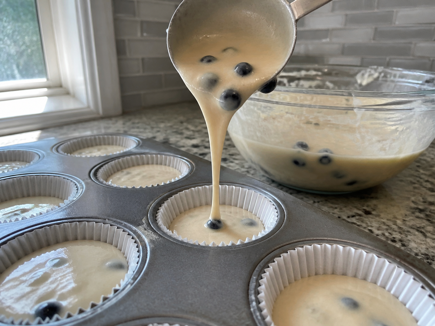 Thin blueberry muffin batter flowing into a lined muffin cup