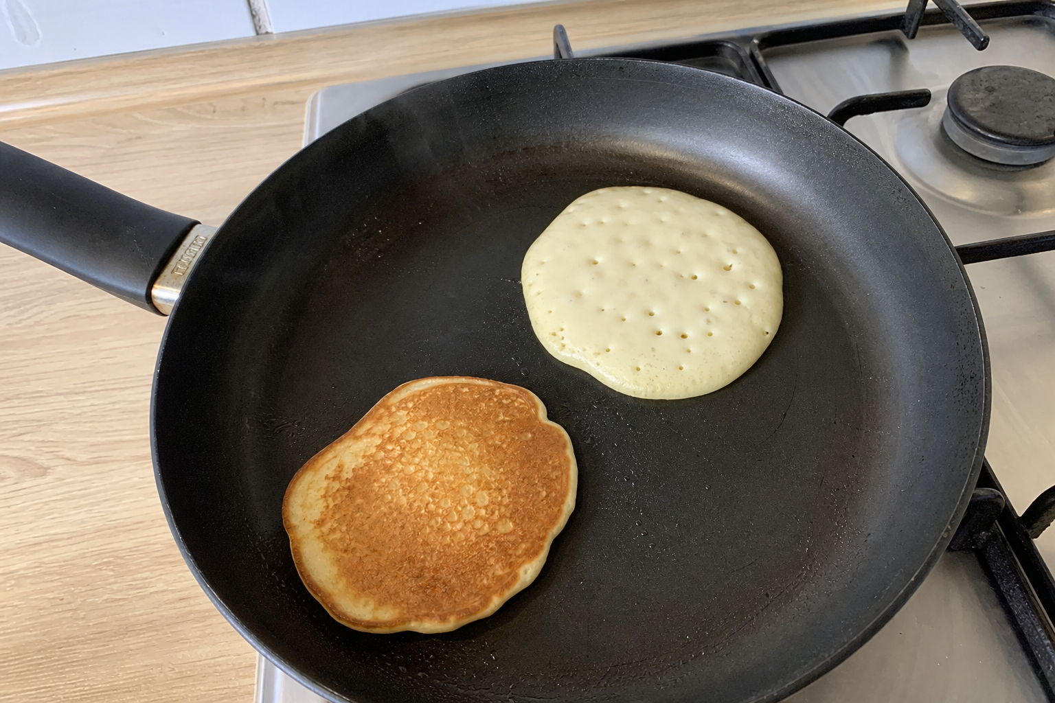Pancakes at different stages of cooking in a dark skillet