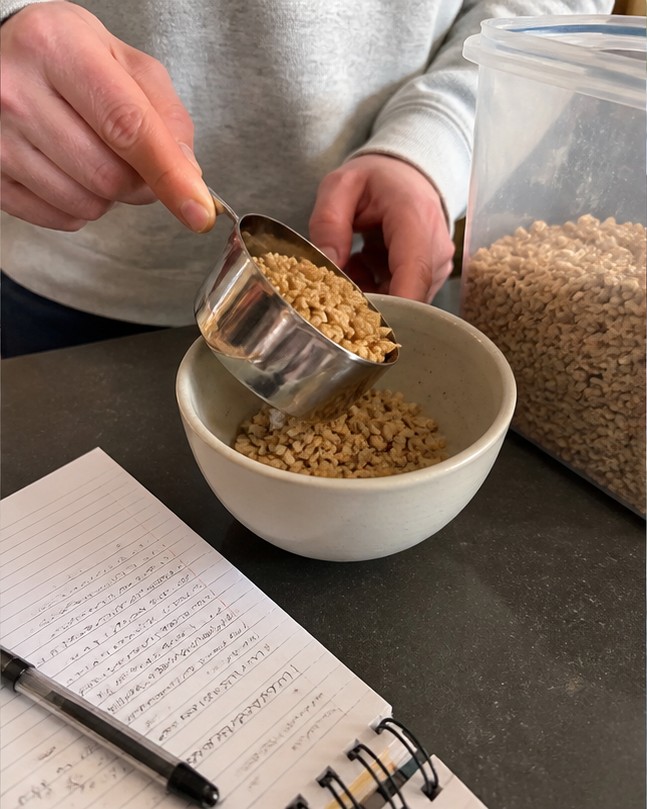 Cereal being poured into a bowl with plain yogurt and banana slices