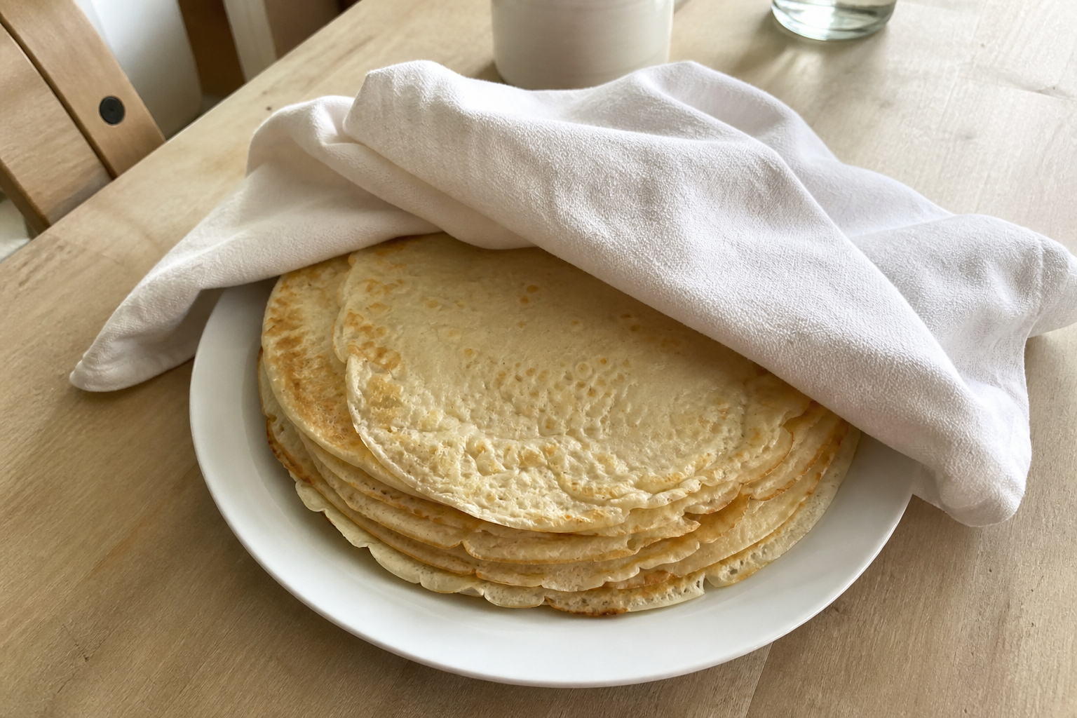 A warm stack of plain crepes covered loosely with a cotton tea towel
