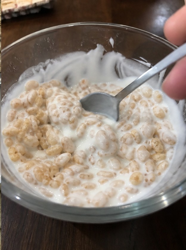 Cereal being poured into a bowl with plain yogurt and banana slices
