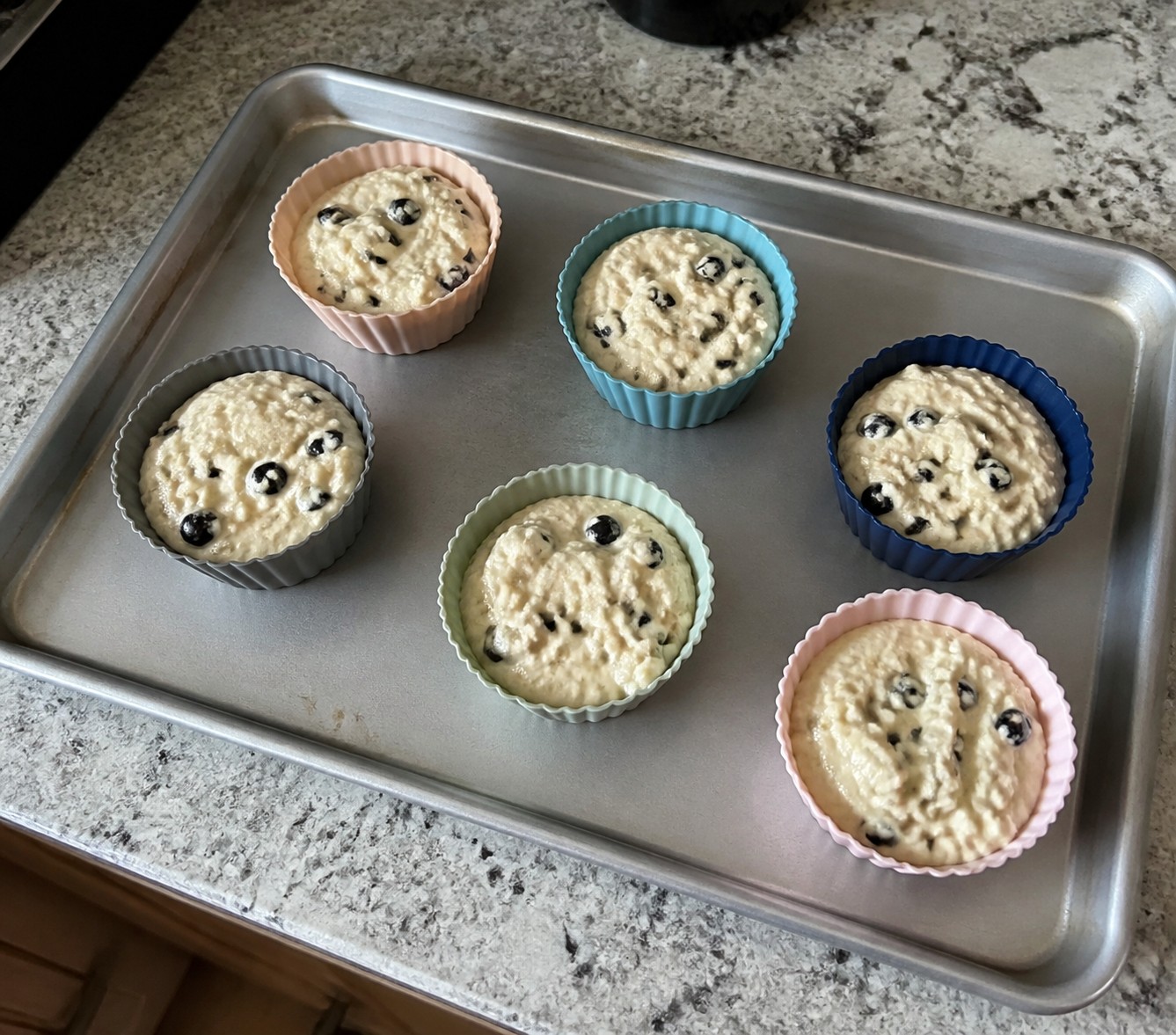 Freestanding silicone muffin cups filled with batter on a metal baking sheet