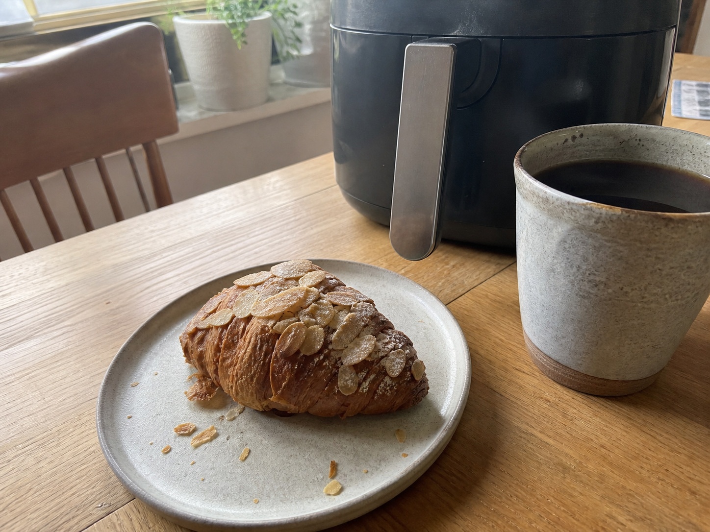 A flaky croissant on a casual morning kitchen table beside an air fryer