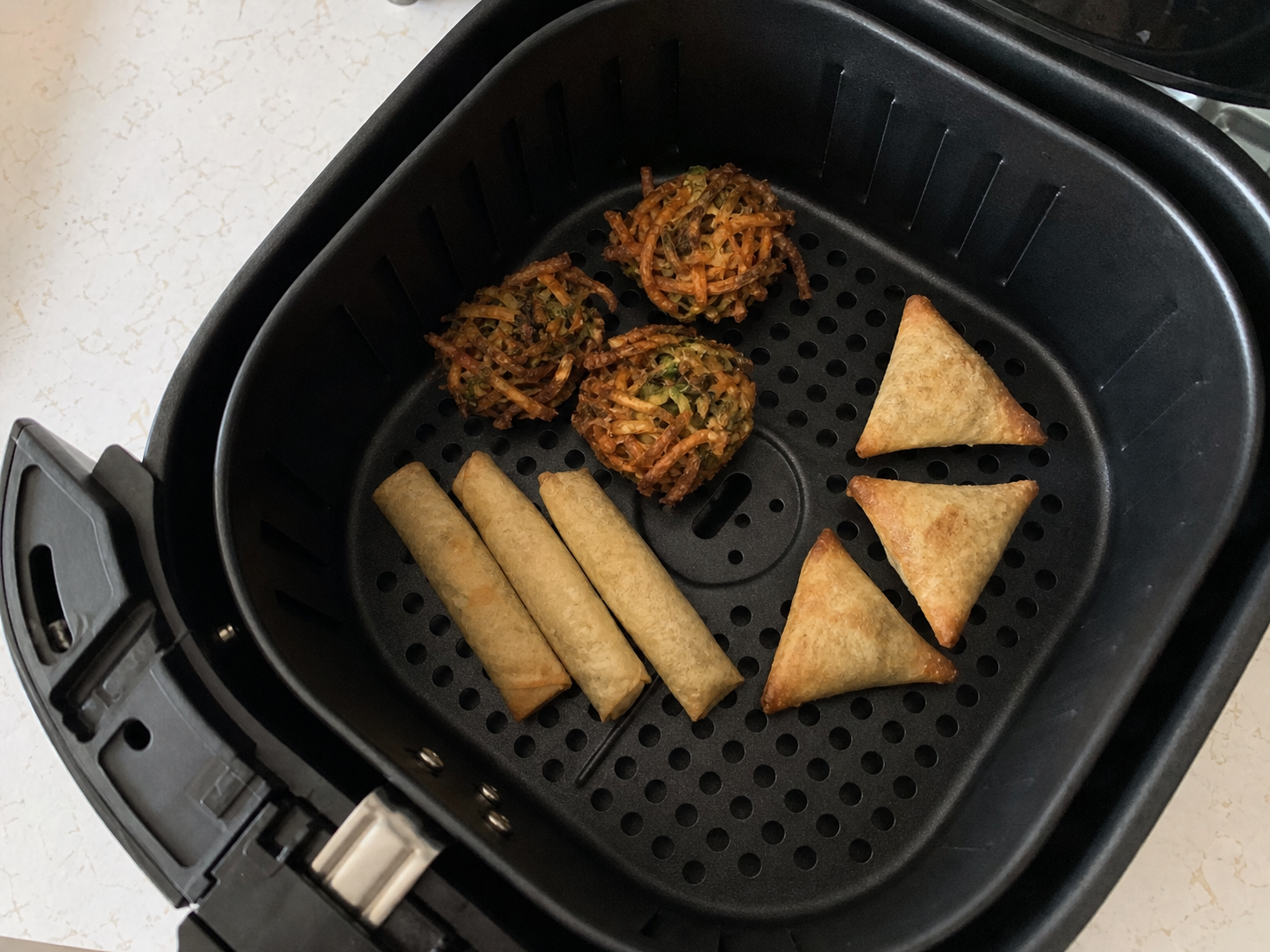 Crisp spring rolls, vegetable nests and samosas in an air-fryer basket
