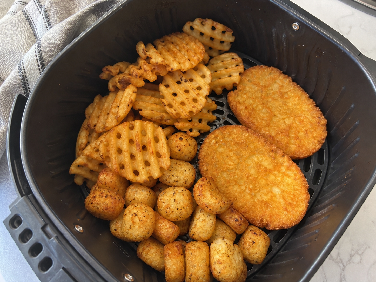 Waffle fries and hash brown patties in an air-fryer basket