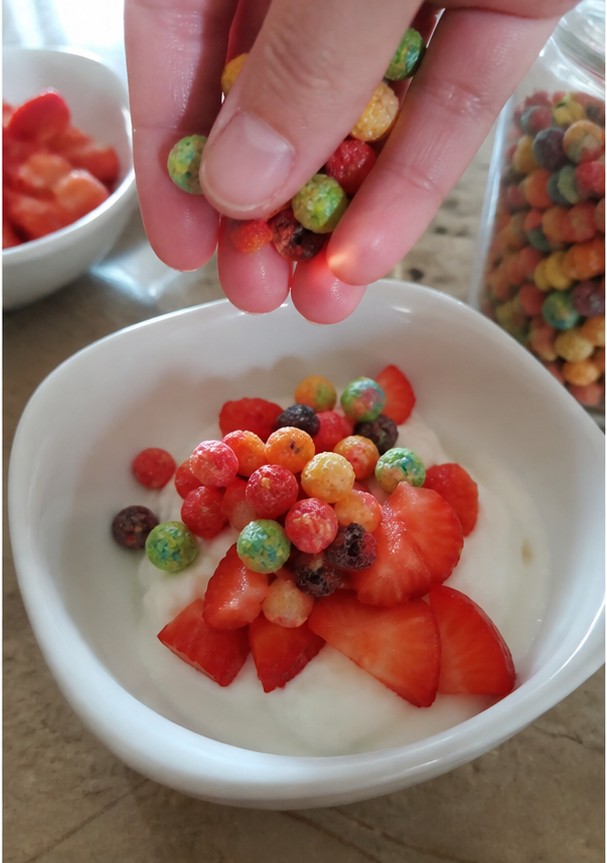 Cereal being poured into a bowl with plain yogurt and banana slices