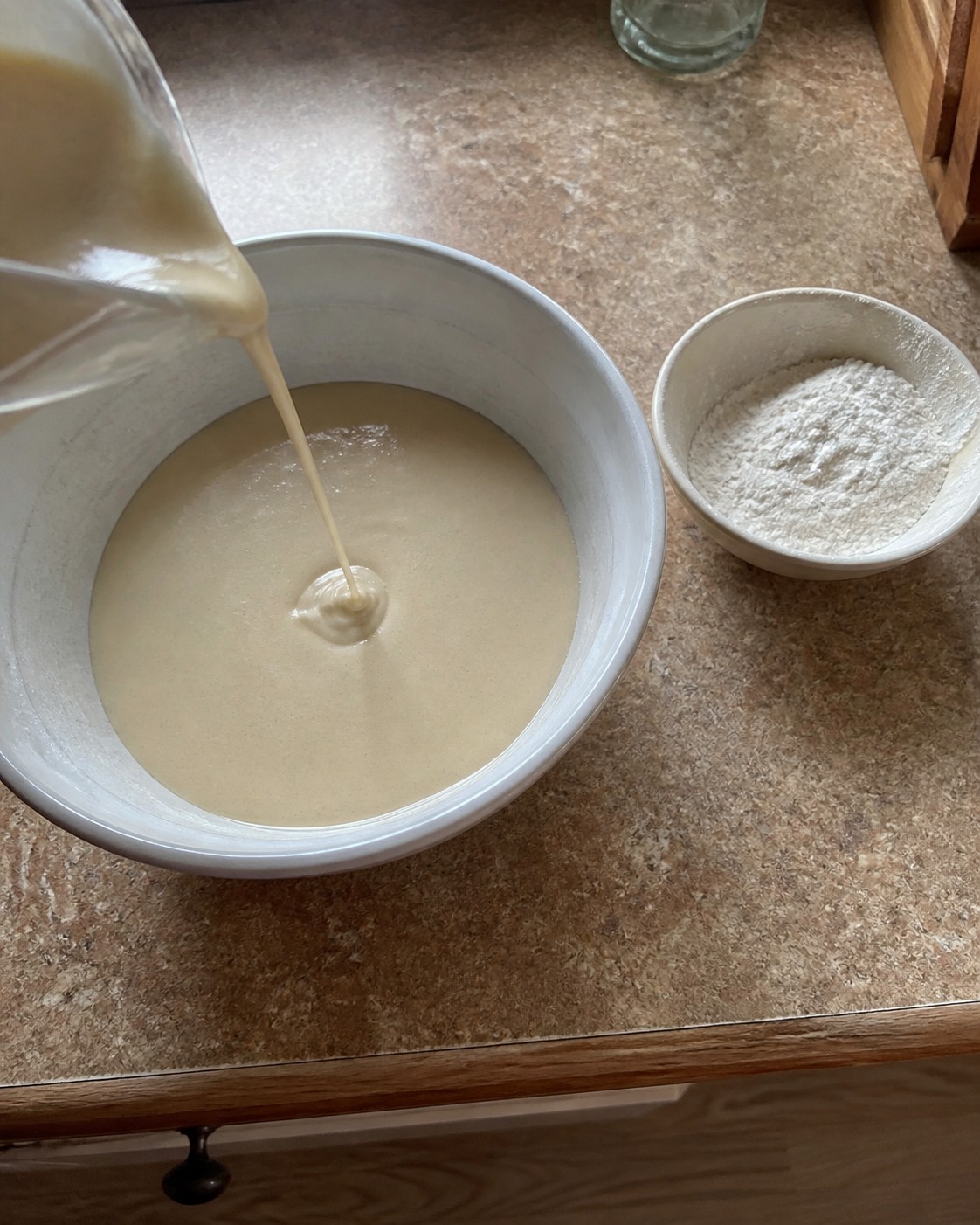 Runny waffle batter pouring from a measuring cup beside flour