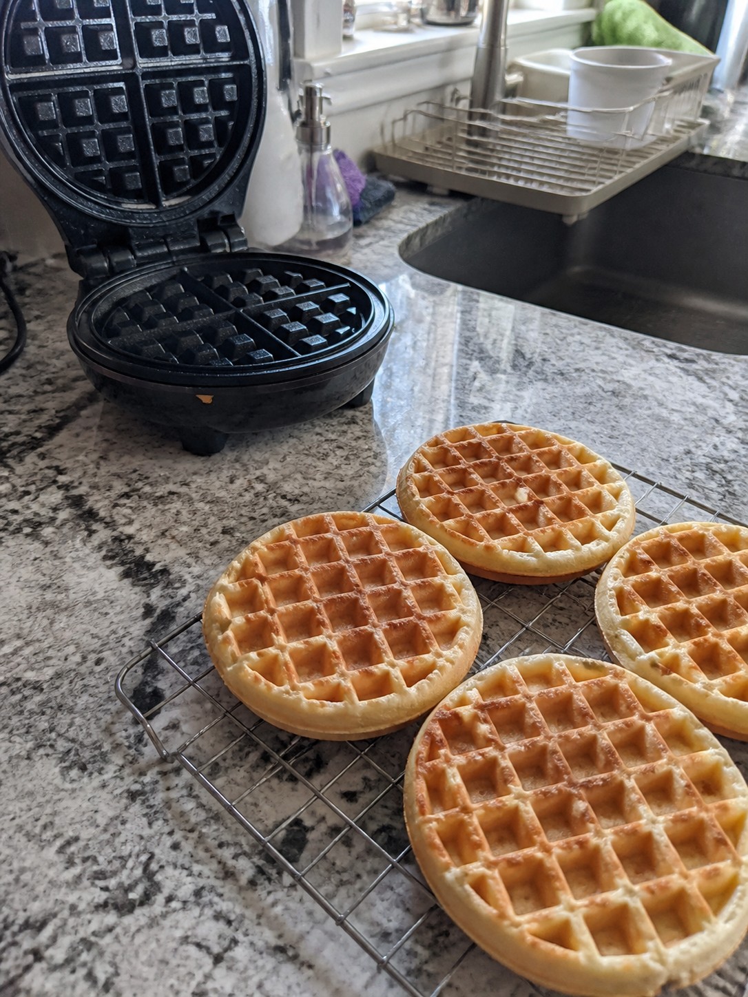 Fresh waffles cooling separately on a wire rack beside a waffle maker
