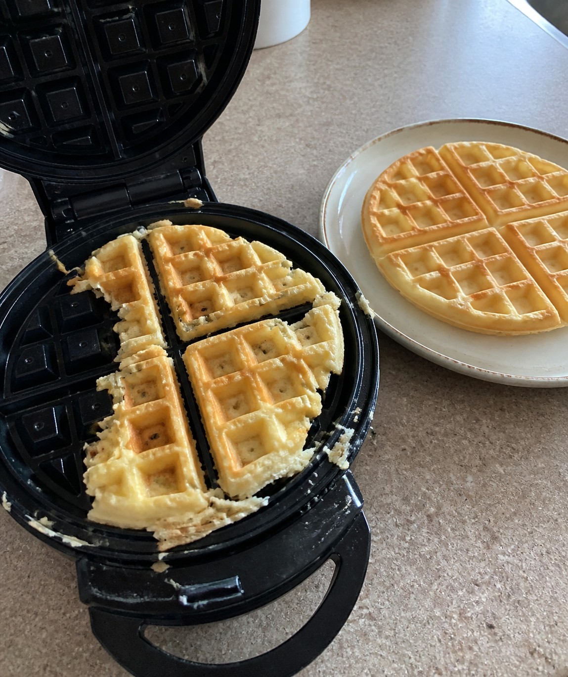 A torn waffle stuck inside an open waffle maker